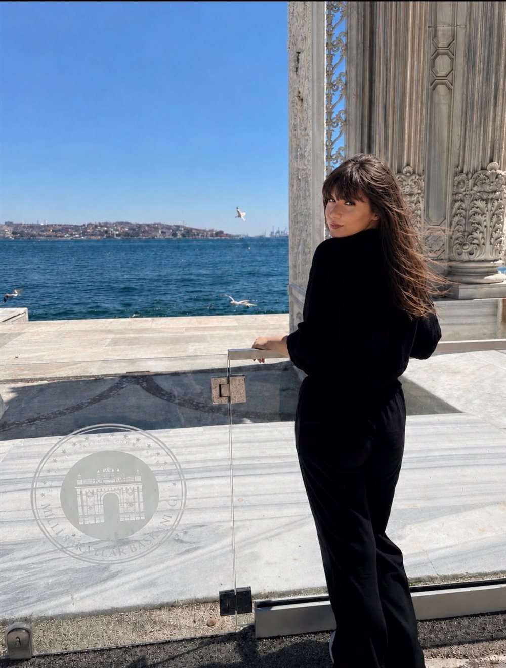 Alexandra Dinu, English tutor and 12th-grade student at Liceul Tehnologic Turceni, smiling over her shoulder by the sea